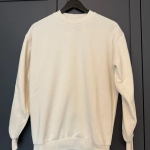 Beige sweatshirt från SMOG XS - Enkel och stilren biege sweatshirt från SMOG i relaxed fit. Tröjan har rund halsringning, ribbade muddar vid ärmslut och nederkant samt lång ärm. Något nopprig