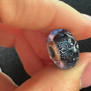Pandora blå glittrig berlock - Säljer en snygg Pandora-berlock i blått glas med glittrig effekt och silverdetaljer. Berlocken har rund form och passar perfekt till armband från Pandora. Märkt med 925 silver och Pandora-logga på kanten.