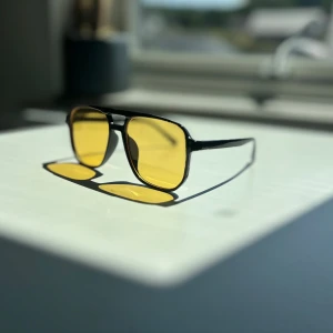 Svarta solglasögon med gula glas - Snygga solglasögon med svart båge och fyrkantiga, gula glas. Ramen är tunn och stilren, vilket ger en modern vibe. Perfekta för dig som vill sticka ut med en cool accessoar i sommar.