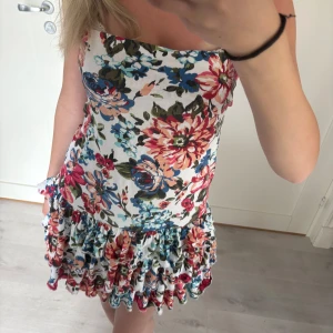 Blommig volangklänning - Supersöt kort klänning med färgglatt blommönster. Klänningen har volanger nertill och är ärmlös. Perfekt för sommarens alla tillfällen och ger en riktigt fräsch look 💕