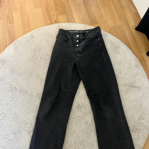 Svarta högmidjade jeans  - Säljer ett par svarta wide leg jeans med hög midja och raka ben. Jeansen har klassisk femficksdesign, knäppning med knappar och är tillverkade i bomull. Köpta på bik bok. Bra skick. 