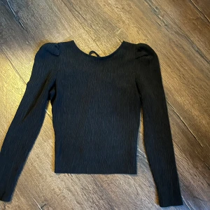 Svart långärmad topp med snörning - Säljer en svart långärmad topp med puffiga axlar och snörning bak vid ryggen! Toppen är i ett ribbat tyg och har ett väldigt skönt material så man kan använda tröjan under en dag💓 Supersnygg!