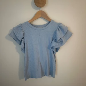 Ljusblå ribbad topp med volangärm Zara - Supersöt ljusblå ribbad topp från Zara med korta volangärmar som ger en extra touch.