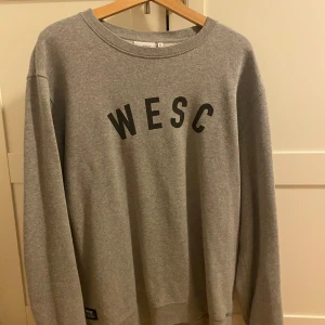 Grå sweatshirt från WESC XL - Säljer en grå sweatshirt från WESC i storlek XL. Tröjan har rund halsringning, svart tryck med WESC på bröstet och är tillverkad i mjuk bomullsmix. Perfekt för en chill och avslappnad stil.