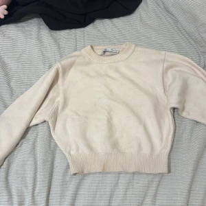 Beige stickad tröja från Zara - En stilren beige stickad tröja från Zara i storlek S. Tröjan har rund halsringning, ribbade muddar och är långärmad. Perfekt för lager-på-lager och enkel att matcha med jeans eller kjol. Mjuk och skön känsla som passar till många looks.