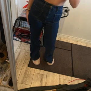 Mörkblå high waist jeans med raka ben - Säljer ett par mörkblå jeans med hög midja och raka ben. Byxorna har stora fickor fram och bak, klassisk jeansknäppning och är i ett mjukt denimtyg. Perfekta för dig som gillar en clean och tidlös look.