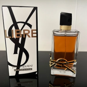 Yves Saint Laurent Libre Intense 90ml - YSL Libre Eau de Parfum Intense i en lyxig, rektangulär glasflaska med guldiga detaljer och svart asymmetrisk kork. Doften är djup och bärnstensfärgad, och flaskan pryds av Denise ikoniska YSL-loggan i metall. Kommer med originalkartong.