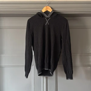 Svart kashmirhoodie från Falconeri - Mjuk och lyxig svart hoodie i kashmir från Falconeri. Tröjan har långa ärmar, huva med grå insida och en diskret grå X-detalj och vid halsen och armen. Perfekt för dig som gillar stilren och bekväm design med premiumkänsla. Har ett litet hål under armhålan. Inget som märks. Storlek 48 motsvarar S. 