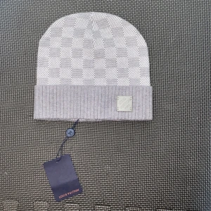 Louis Vuitton mössa - Exklusiv grå mössa från Louis Vuitton med klassiskt rutigt mönster och ribbad uppvikt kant. Mössan har en diskret Louis Vuitton-plakett framtill och är tillverkad i mjukt material som känns lyxigt mot huden. Perfekt accessoar för att lyfta din vinterstil.