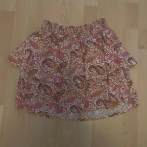 Mönstrad kortkjol från Gina Tricot - Kortkjol från Gina Tricot i bomull med paisleyinspirerat mönster i rosa, orange och vitt. Kjolen har resår i midjan för en bekväm passform och är perfekt för dig som gillar färg och mönster. Kjolen passar alla storlekar från xs till L