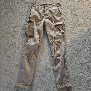 Beige cargopants från Jack and Jones - Säljer ett par beige cargopants med flera stora fickor på sidorna. Byxorna har rak passform och är tillverkade i ett mjukt bomullstyg. Perfekta för dig som gillar en avslappnad och funktionell stil. Original pris: 800kr