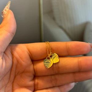 Tiffany guldhalsband med hjärtan -  två hjärtformade berlocker, varav en är graverad med klassisk Tiffany-text. Kedjan är tunn och elegant, perfekt för att ge en lyxig touch till din stil. Kommer i den ikoniska turkosa asken.