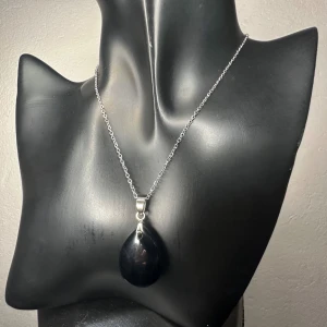 Nytt halsband i rostfritt stål med äkta droppformad obsidian - Ädelsten för skydd & balans - Elegant halsband med droppformat hänge i obsidian (ca 3,5 x 2 cm) och kedja i rostfritt stål (44 + 5 cm). Obsidian är känd som en kraftfull skyddssten som sägs absorbera negativ energi och hjälpa bäraren att hitta inre balans och klarhet. Den svarta ytan ger smycket en tidlös och kraftfull känsla, perfekt för både vardag och fest.  Halsbandet är nytt och oanvänt. Prutning ej möjlig, men jag erbjuder rabatt vid köp av flera saker. Jag rensar smyckesskrin och garderob – kika på mina andra annonser