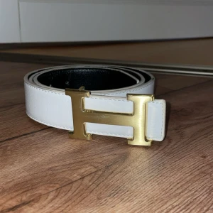 Vitt H-skärp med guldfärgat H-spänne - Snyggt vitt bälte ikoniskt H-spänne i guldmetall. Perfekt accessoar för att lyfta din outfit med en lyxig touch och klassisk design. Storlek 110 cm. Bältet är ej original.