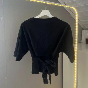 Back tie topp Nelly - Back tie topp från Nelly i storlek XS. Toppen har korta ärmar, rund halsringning och knytband i ryggen. Passar perfekt till både vardag och fest!