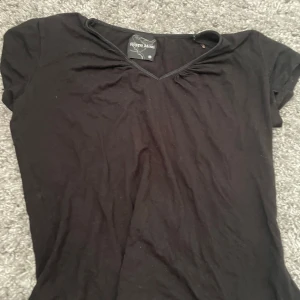Svart v-ringad topp Filippa Mossi - En svart, enkel och stilren topp från Filippa Mossi med v-ringning och korta ärmar. Perfekt att matcha med jeans eller kjol för en clean look. Mjuk och skön känsla, passar dig som gillar minimalistisk stil.