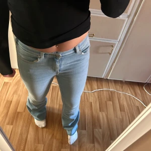 Ljusblå bootcut jeans - Säljer ett par ljusblå jeans med bootcut-modell och klassisk femficksdesign. Jeansen har låg midja och är tillverkade i mjukt denimtyg som sitter snyggt över höfterna och låren. 