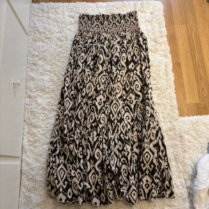  långkjol med mönster - Säljer en flowy långkjol med brun/beiget grafiskt mönster. Kjolen har smock i midjan för en bekväm passform och är tillverkad i ett lätt tyg som ger snyggt fall❤️