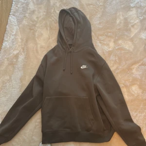 Brun Nike hoodie med huva, strl L - Säljer en brun hoodie från Nike i storlek L. Tröjan har klassisk huva med snörning, stor magficka och Nike-logga broderad i vitt på bröstet. Mjuk insida i fleece och långärmad modell, perfekt för kyliga dagar.