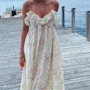 Lång blommig sommarklänning med volang - Superfin långklänning med tunna axelband och volang vid bysten. Klänningen är vit med blommigt mönster i ljusrosa, grönt och gult. Populär klänning som fortfarande är i mycket bra skick! 💕💕
