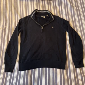 Mörkblå stickad half zip-tröja GANT - Snygg mörkblå stickad tröja från GANT med halv dragkedja och broderad logga på bröstet. Tröjan har ribbade muddar och krage med vit randig detalj. Passar riktigt bra till allt året runt, perfekt för dig som gillar klassisk och stilren look. Skick: 8,5/10 Hör gärna av dig vid intresse om fler bilder eller frågor😊