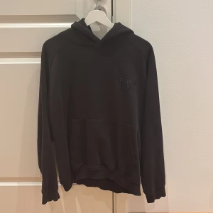 Svart hoodie Training Dept. - Svart hoodie med trycket 'TRAINING DEPT.' på både bröstet och ryggen. Klassisk känguruficka framtill, huva och långa ärmar. Skön och avslappnad passform, perfekt för chill eller träning. Materialet känns mjukt och är troligtvis bomull eller bomullsblandning.