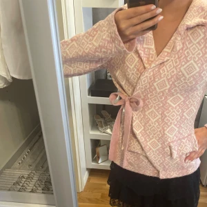 Ljusrosa kofta - Superfin stickad kofta i ljusrosa och vitt från Lely Wood med snyggt geometriskt mönster, krage och knytband. Finns ett litet hål (bild 5), men är på insidan av armen så syns inte vid användning, men går annars lätt att sy! Är justerbar i midjan som ger en perfekt passform, passar storlek S/M.