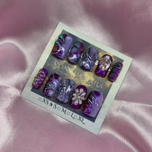AmethystTrap (S);Short Square;Curved - Snygga press-on naglar i lila och mörklila med metallicblå och silvriga detaljer. Några naglar har 3D-blommor och glittereffekter. Formen är squareformad och designen är handmålad med swirl-mönster och stenar. Perfekt för dig som vill sticka ut med coola naglar.