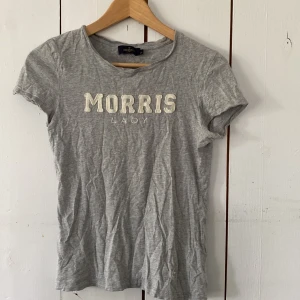 Grå t-shirt från Morris Lady XS - Snygg grå t-shirt från Morris Lady i mjuk bomull med broderad vit text på bröstet. Klassisk rund halsringning och korta ärmar. Perfekt till jeans eller shorts för en chill look.