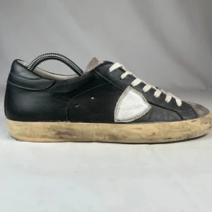 Philippe models  - Snygga svarta sneakers med grå mocka på tån och plös, vita snören och en vit detalj på sidan. Skorna har en vintage-inspirerad, smutsad sula och är tillverkade i skinn och mocka. Perfekta för dig som gillar en avslappnad och trendig look.