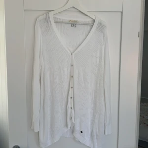 Vit kofta från Odd Molly, stl 4 - Snygg vit kofta från Odd Molly med v-ringning och knappar framtill. Koftan har ett diskret blommigt mönster i stickningen och långa ärmar. Perfekt för lager-på-lager och ger en fräsch look till din outfit.