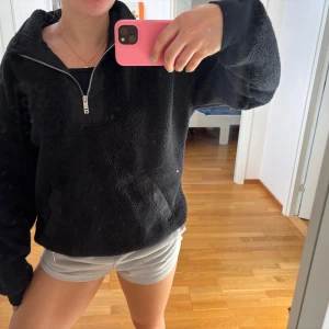 Svart fleece half zip från SOC - Mysig svart fleece-tröja från SOC i storlek M. Tröjan har en praktisk half zip-dragkedja framtill, stora fickor och är tillverkad i mjukt fleecematerial. Perfekt för kyliga dagar och enkel att slänga på sig över en t-shirt.