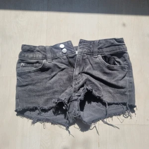 Grå jeansshorts med fransig kant - Snygga grå jeansshorts från Cubus i storlek 158. De har rå, fransig kant nertill och slitna detaljer för en cool look. Klassisk femficksmodell med knappar och dragkedja framtill samt fickor med lock bak. Perfekta för sommardagar och festivaler.
