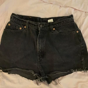 Svarta Levi's 512 jeansshorts - Svarta jeansshorts från Levi's modell 512 med hög midja och råa, fransiga benslut. Klassisk femficksdesign, knapp och dragkedja framtill samt Levi's patch bak. Perfekta för en avslappnad och cool stil. OPS!!! Vet ej om dem är äkta då jag köpte dem secondhand men skulle inte tro att dem är äkta!💋🥂💐