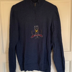 Blå halvzip tröja från Lyle & Scott - Mörkblå långärmad tröja från Lyle & Scott med broderad logga och emblem på bröstet. Är en liten tråd som ligger fel på emblemet dock varit så sedan ny. Och inget man ser när tröjan sitter på. Säljer den då den har blevit för liten för mig