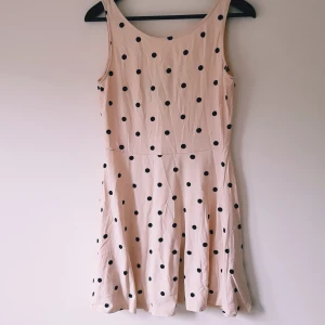 Prickig kort klänning från H&M Divided strl 42 - Supersöt ljusbeige kort klänning från H&M Divided med svarta prickar. Ärmlös modell med rundad hals och lätt utställd kjol. Perfekt för dig som gillar retrovibbar och lekfull stil.  Helt & fint skick dock tvättludd