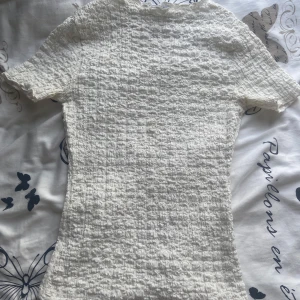 Vit smockad topp från Zara - Säljer denna super fina vit t-shirt från Zara i storlek S med struktur. Den är figursydd och har stretchigt material 