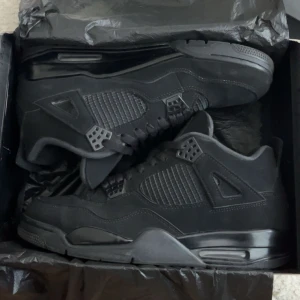 Nike Air Jordan 4 Retro Black Cat - Säljer ett par Nike Air Jordan 4 Retro Black Cat i helsvart mocka och syntet. Klassisk siluett med meshpaneler, snörning och ikoniska detaljer på hälen. Perfekta för dig som gillar stilrena och tidlösa sneakers med streetkänsla.