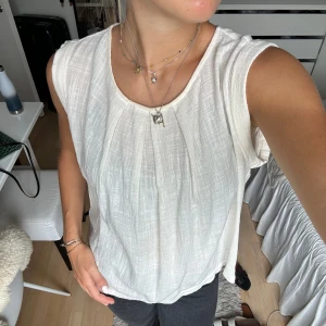 Vit ärmlös blus i luftig bomull - Säljer en vit ärmlös blus med snygga veck framtill. Perfekt till sommaren!  Köpt på Åhléns