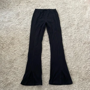 Svarta bootcut byxor med slits - Snygga svarta bootcut byxor med slits framtill vid bensluten. Byxorna har en tight passform upptill och vida ben nertill, vilket ger en riktigt trendig siluett. Perfekta att styla med sneakers eller boots för en cool look.