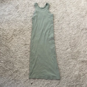Ljusgrön ärmlös långklänning - Snygg och enkel ljusgrön långklänning med ärmlös design och rund halsringning. Klänningen har en rak passform och är tillverkad i mjukt bomullstyg, perfekt för varma dagar. Stilren och minimalistisk look som är lätt att matcha.