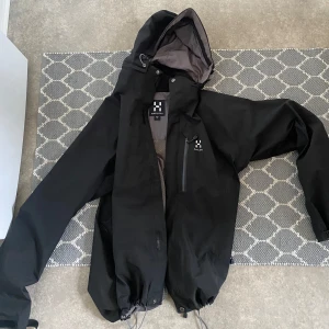 Svart vindjacka från Haglöfs, M - Svart vindjacka från Haglöfs i storlek (M)Jackan har en bröstficka med dragkedja  Perfekt för blåsiga och regniga dagar. Använd max 10 gånger så jackan är i väldigt fint skick 