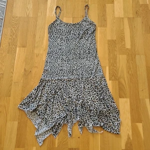 Leopardmönstrad kortklänning med volang - Säljer en kort klänning med leopardmönster och smala axelband. Klänningen har en asymmetrisk volangkant nertill. Supertunnt material som är perfekt för varma sommardagar. Storlek M, men står ej märke.