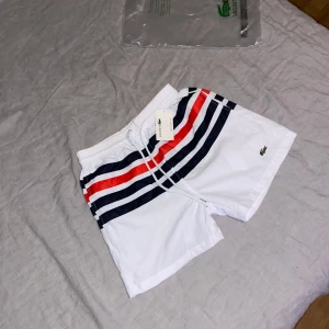 Vita randiga badshorts från Lacoste - Hej, Jag säljer mina Lacoste shorts i storlek S/M. Shortsen är helt oanvända och i ny skick👍 Hör gärna av dig om du har några frågor eller funderingar 😊