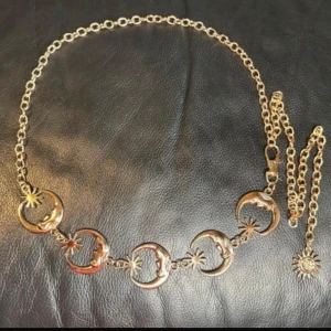 Guldfärgat kedjebälte med månar & solar - perfekt för Wicca, witchy, boho & alt. Looks - Säljer ett drömmigt kedjebälte i guldfärgad metall med månskäror och små solar. Ett uttrycksfullt accessoar som ger en mystisk, lite vintageinspirerad känsla till vilken outfit som helst. Justerbar längd ca 110 cm, månskäror ca 3,5 cm. Stängs med karbinhake och har dekorativt solhänge. Snyggt över klänning, kjol, jeans eller crop top – perfekt för festival, vardag eller styling. Oanvänt och i mycket fint skick. Prutning accepteras inte, men jag erbjuder bra rabatt vid köp av flera saker. Kolla g