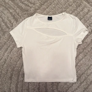 Vit ribbad topp med cut out Gina Tricot - Vit ribbad topp från Gina Tricot i storlek S. Modellen är croppad med korta ärmar och har en snygg cut out-detalj framtill vid bröstet. Tunt och stretchigt material som känns skönt mot huden. Perfekt för dig som gillar trendiga detaljer och enkel stil.