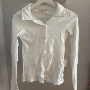 Tröja  - En vit ribbad tröja med knappar och krage, väldigt snygg! Från Nelly i storlek XS, använd ett fåtal gånger🥰