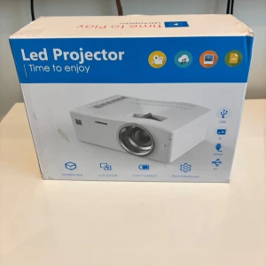 Led projector  - Bilderna visar en LED-projektor i originalförpackning, inte en bok. Produkten är kompakt och portabel, med stöd för flera filformat och anslutningar som USB, HDMI och AV. Perfekt för filmkvällar, gaming eller presentationer hemma eller med vänner.