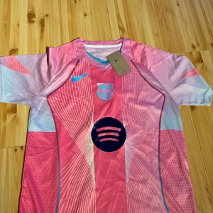 FC Barcelona rosa matchtröja Nike - Passar både M och L Snygg FC Barcelona fotbollströja från Nike i rosa och ljusblå toner. Tröjan har korta ärmar, tunnt funktionsmaterial och coola vita linjemönster framtill. Klubblogga och Nike-logga i blått, samt Spotify-logga på bröstet. Perfekt för dig som vill sticka ut på planen. 