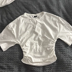 Vit t-shirt med snörning från Gina Tricot - Vit t-shirt från Gina Tricot i storlek S. Modellen har korta ärmar och cool snörningsdetalj på sidan som ger en snygg, lite croppad look. Tillverkad i mjuk bomull med rund halsringning. Perfekt för dig som gillar stilrena och trendiga plagg.